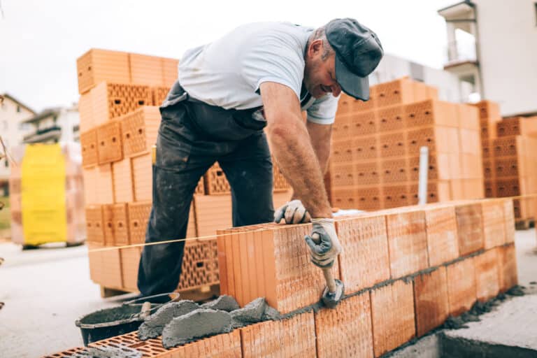 industrial worker building exterior walls, using hammer for laying bricks in cement